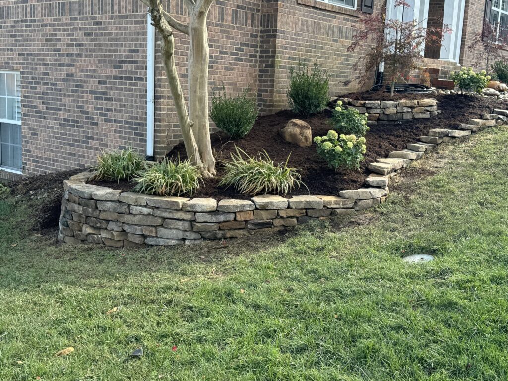 Tiered stone retaining wall supporting a landscaped slope in a residential backyard.