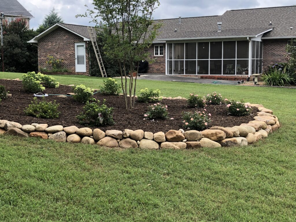 Tiered stone retaining wall supporting a landscaped slope in a residential backyard.